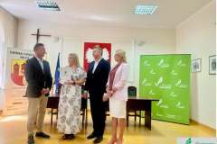 Grupa samorządowców stojących przy stole z flagą Unii Europejskiej i godłem Polski na wydarzeniu Granty Sołeckie Choszczno.