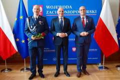 Wojewoda zachodniopomorski oraz odznaczony funkcjonariusлец w mundurze stojący na tle flag podczas uroczystości Medal za długoletnią służbę.